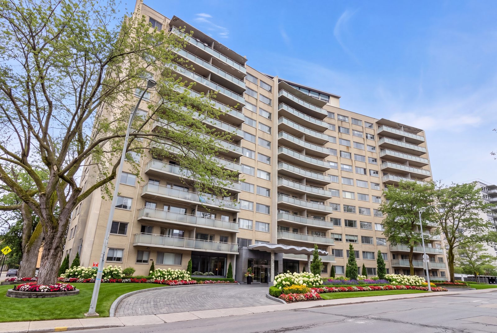 Le Royal Westmount iL Palazzo au 250 avenue Clarke : façade aux balcons incurvés, marquise ondulée à l'entrée principale et parterres fleuris en été